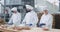 Very charismatic baker woman with a large smile and her colleagues bakers men forming the dough to baking the bread