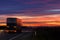 A very colorful sunset and a moving blurred truck on an asphalt road