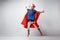 Very excited little girl dressed like superhero jumping alongside the white wall.