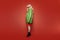 Very fashionable photo of a girl on a red background in flight. A blonde in a bright green raincoat, red glasses and a red dress