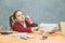 Very good schoolgirl girl sitting at the table. During this, he holds his hand on the books that stand on the table