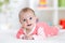 Very happy laughing baby in pink clothes lying on his belly. Infant looking straight at the camera