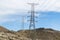 A very long and tall electric supply chain of tall metal towers on the top of dried mountains