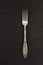 Very old rusty vintage silver fork isolated on a black cement texture background