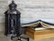 A very old silver lantern, a pile of old books, a pair of glasses on bleached oak background.