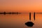 Very orange sunset with pilings and logs reflect in glassy river surface