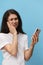 a very pensive woman stands on a blue background in a white T-shirt with a fashionable phone in her hands and looks at