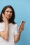 a very pensive woman stands on a blue background in a white T-shirt with a fashionable phone in her hands and looks at