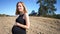 Very pregnant blonde woman, hand resting on stomach, happy expression, standing on dirt field, fallen tree and roots in background