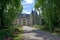 a very pretty large old style house surrounded by trees and flowers