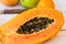 Very ripe juicy papaya cut in half on wood kitchen table with citrus fruits, apples, knife