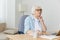 a very serious, stylish, elderly woman is sitting at home at her laptop and working intently with her hand near her face