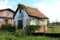 Very small abandoned old red brick family house ruins with broken windows and cracked facade partially covered with crawler plants