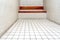 The very sober interior of a prison cell: bare tiled walls and a wooden bench