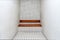 The very sober interior of a prison cell: bare tiled walls and a wooden bench