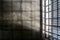 The very sober interior of a prison cell: barred windows with little light coming in and bare concrete walls