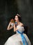 Very tasty. Emotional woman, royal person, queen or princess in white medieval outfit eating burger on dark background