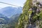 Via ferrata climbing, woman in harness crossing rope bridge in the mountains