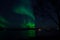 Vibrant aurora borealis over fjord and mountain reflecting in sea