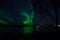 Vibrant aurora borealis over fjord and mountain reflecting on the sea