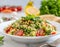 A vibrant bowl of fresh tabbouleh salad garnished with a sprig of mint, surrounded by ingredients like tomatoes and olive oil, set