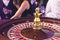 Vibrant casino table with roulette in motion, with casino chips, tokens, the hand of croupier, dollar bill money and a group of