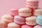 A vibrant collection of assorted pastel french macarons creates a sweet, inviting pile against a pink backdrop, ideal