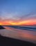 A vibrant colorful sunset over the coastline as waves recede back into the ocean under orange and pink clouds.