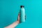 Vibrant cyan backdrop emphasizes female hand clutching steel water bottle