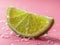 A vibrant green slice of lime delicately balanced on a soft pink surface, creating a contrasting and visually appealing