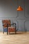 Vibrant orange ceiling light and a comfortable armchair with a colorful boho pattern in a gray living room interior with place for