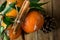 Vibrant Orange Tangerines on Branches Green Leaves Cinnamon Sticks tied with Twine Pine Cone Wood Background. Christmas