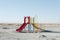 A vibrant playground set with slides and swings stands out against the barren desert landscape, A playground isolated in the