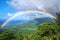 A vibrant rainbow arcs across the sky, creating a colorful contrast against the lush green valley below, A rainbow spanning across