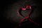 Vibrant red ribbon in the shape of a heart against a stark black background