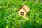 Vibrant springtime background: miniature wooden house standing on a meadow of fresh green grass and vibrant field flowers