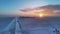 Vibrant sunset on the horizon illuminates a snowy landscape with a truck and its trailer.