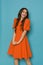 Vibrant young woman is posing in orange cocktail mini dress with puffed short sleeves