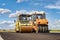 Vibratory road roller lays asphalt on a new road under construction. Close-up of the work of road machinery. Construction work on