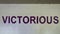 Victorious is painted in bold purple letters on a white brick wall in the parking garage on Victory Park Lane, Dallas, Texas