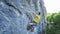 Vide angle view of man rock climber in yellow t-shirt, climbing on a cliff, searching, reaching and gripping hold