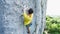 Vide angle view of man rock climber in yellow t-shirt, climbing on a cliff, searching, reaching and gripping hold