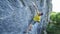 Vide angle view of man rock climber in yellow t-shirt, climbing on a cliff, on tough sport route, resting and chalking