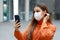 Video calling and Social Distancing. Beautiful young woman in city street wearing protective mask using mobile phone to make video