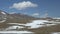 Video of flock of sheep grazing on Altai mountain slope with snow under blue sky and clouds