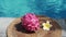 Video footage of red dragon fruit on the edge of swimming pool with white tropical flowers frangipani, bubbling pool blue water