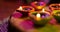 Video of glowing lit diwali candles in circle on woven purple to green surface