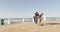 Video of happy african american father learning son how to skateboard on promenade