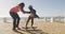 Video of happy african american father learning son how to skateboard on promenade