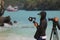 The video photographer or journalist wearing a mask and recording the tourist activities on the beach during the spread of the